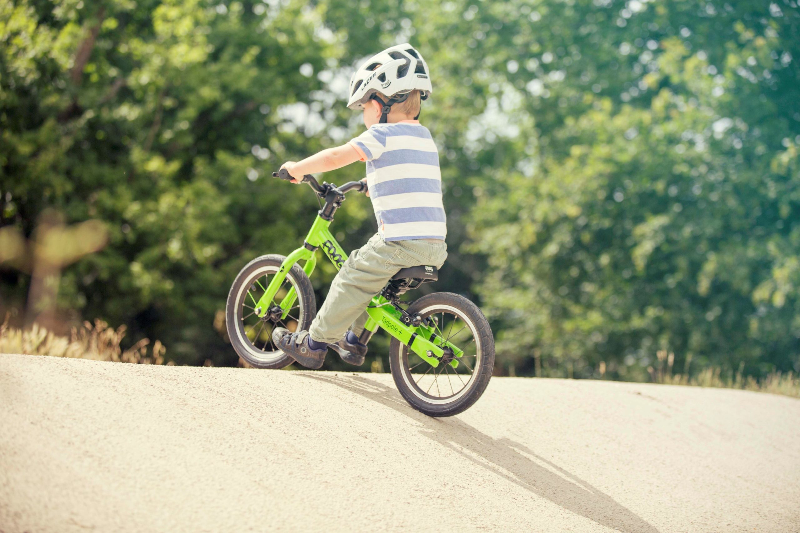 A child riding a green Frog Tadpole Plus bike on a pumptrack